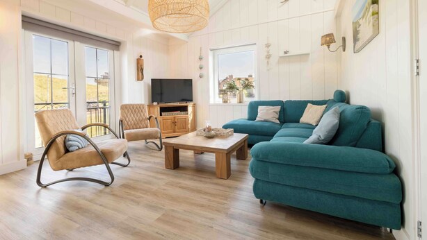 Ein großzügiges Wohnzimmer mit einem türkisfarbenen Sofa, einem Holztisch, einer Korbtrophäe und einem Fernseher auf einer Holzkommode.