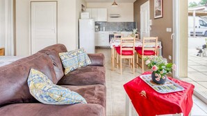 Una sala de estar acogedora con un sofá marrón, una mesa de comedor con sillas rojas y una cocina al fondo.
