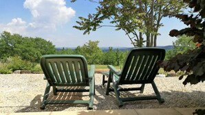 Dos sillas Adirondack verdes mirando a una mesa con vistas a un viñedo y montañas distantes.