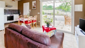 Una sala de estar moderna con un sofá de cuero marrón, un comedor con mesa y sillas, una cocina con estufa y horno, y un ventanal corredizo que da a un patio exterior.