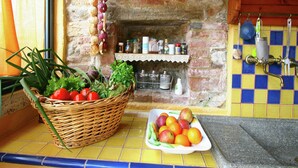 Eine Küche mit Steinwand, Fliesenrückwand, einem Korb frischem Gemüse und einer Schüssel Obst.