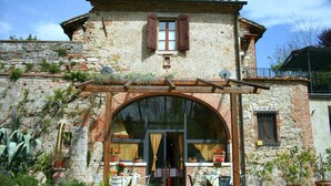 Ein rustikales Steinhaus mit großem Bogenportal, Außenbereich mit Sitzgelegenheiten und Blumentöpfen.