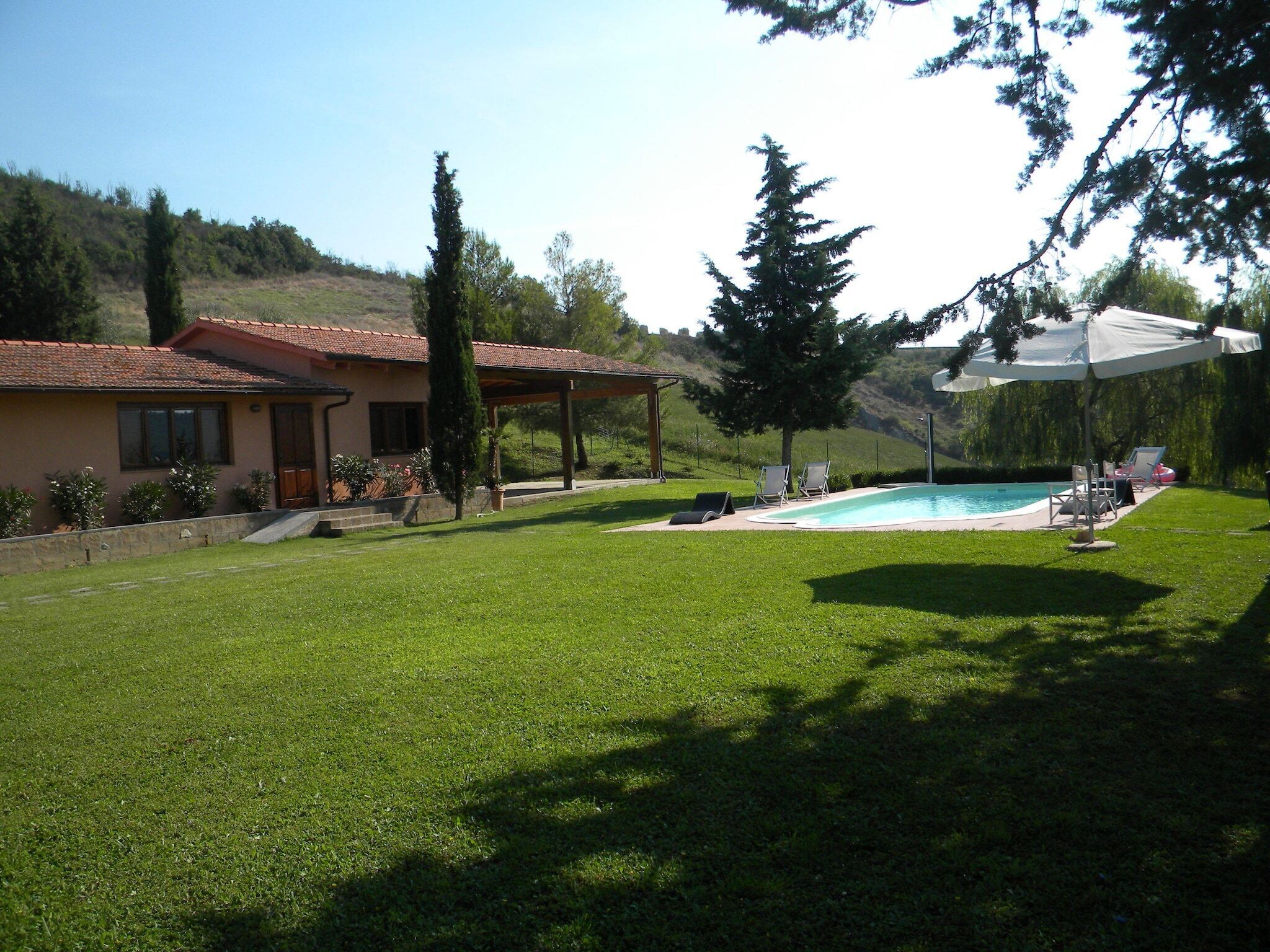 A house with a swimming pool, a covered patio, and a grassy lawn.