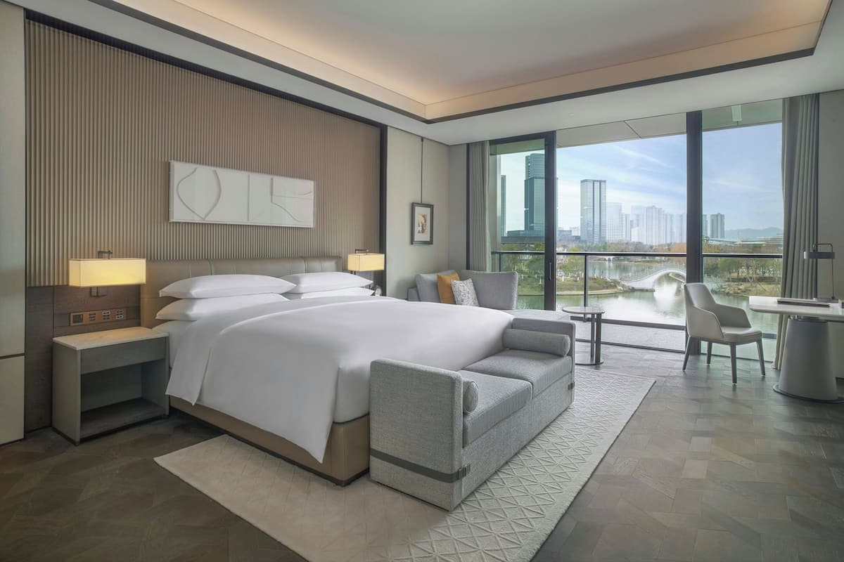 Camera d'albergo moderna con un ampio letto, una scrivania e vista sullo skyline urbano attraverso grandi finestre.