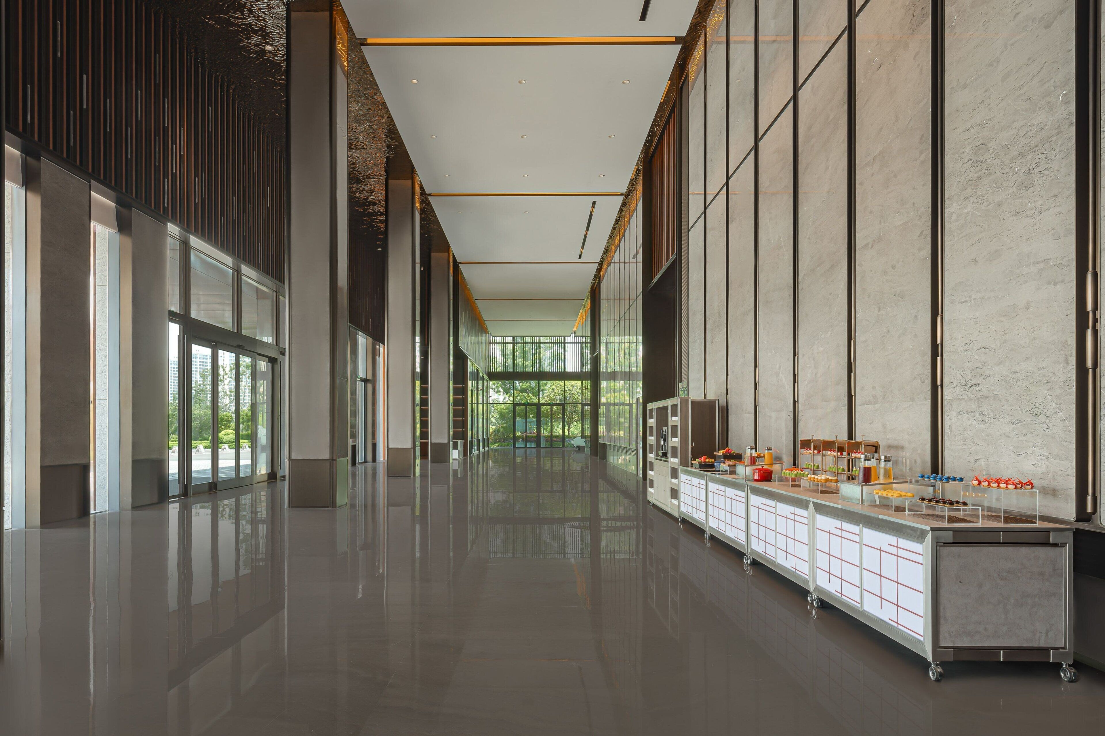 A spacious corridor with a long counter displaying various food items, large windows, and a modern interior design.
