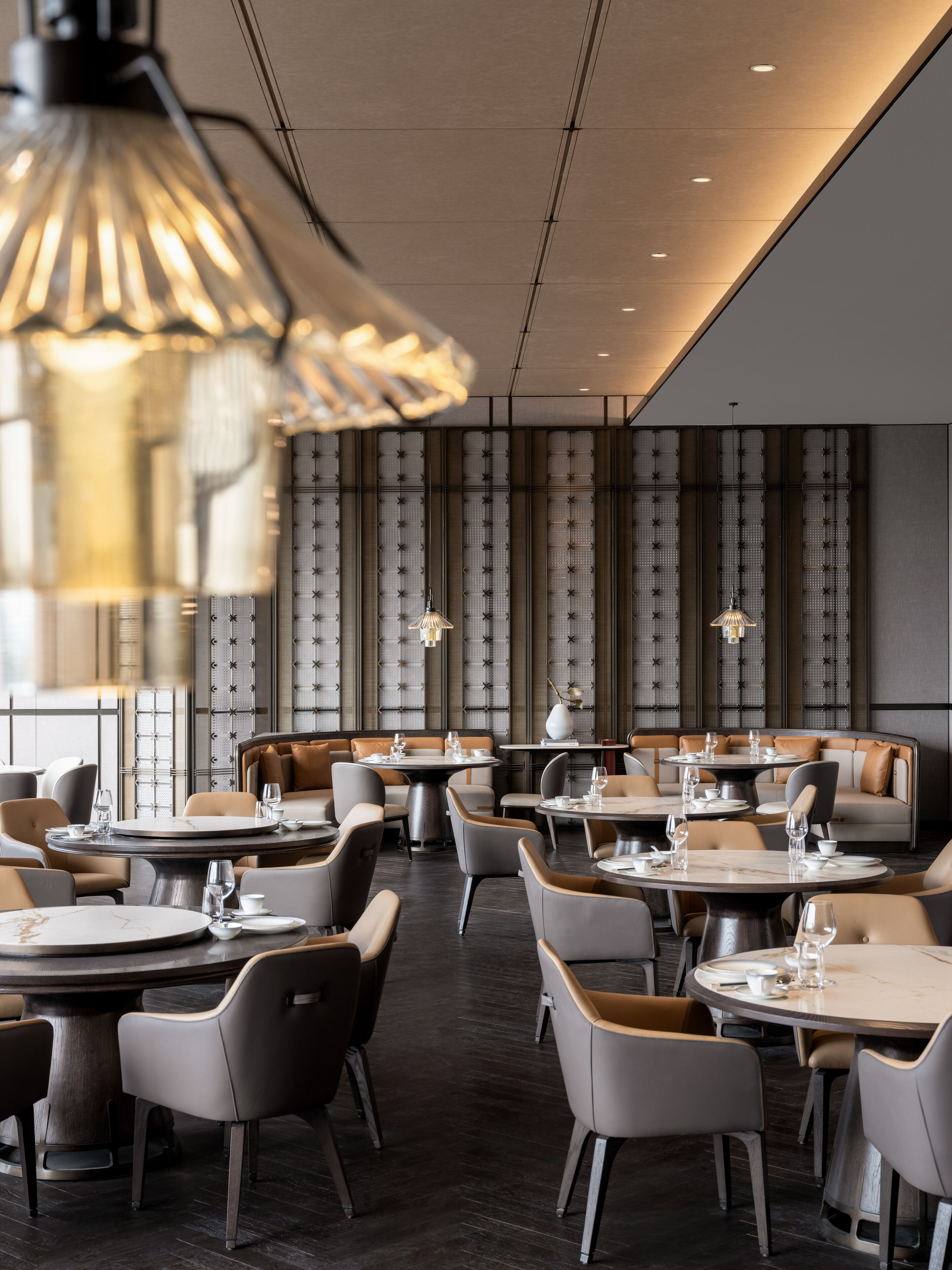 Un interior de restaurante moderno con mesas redondas, asientos acolchados e iluminación colgante.