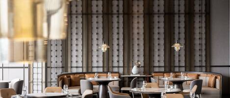 Un interior de restaurante moderno con mesas redondas, asientos acolchados e iluminación colgante.