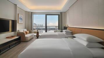 A hotel room with a large bed, a sofa, a TV, and a view of the cityscape.