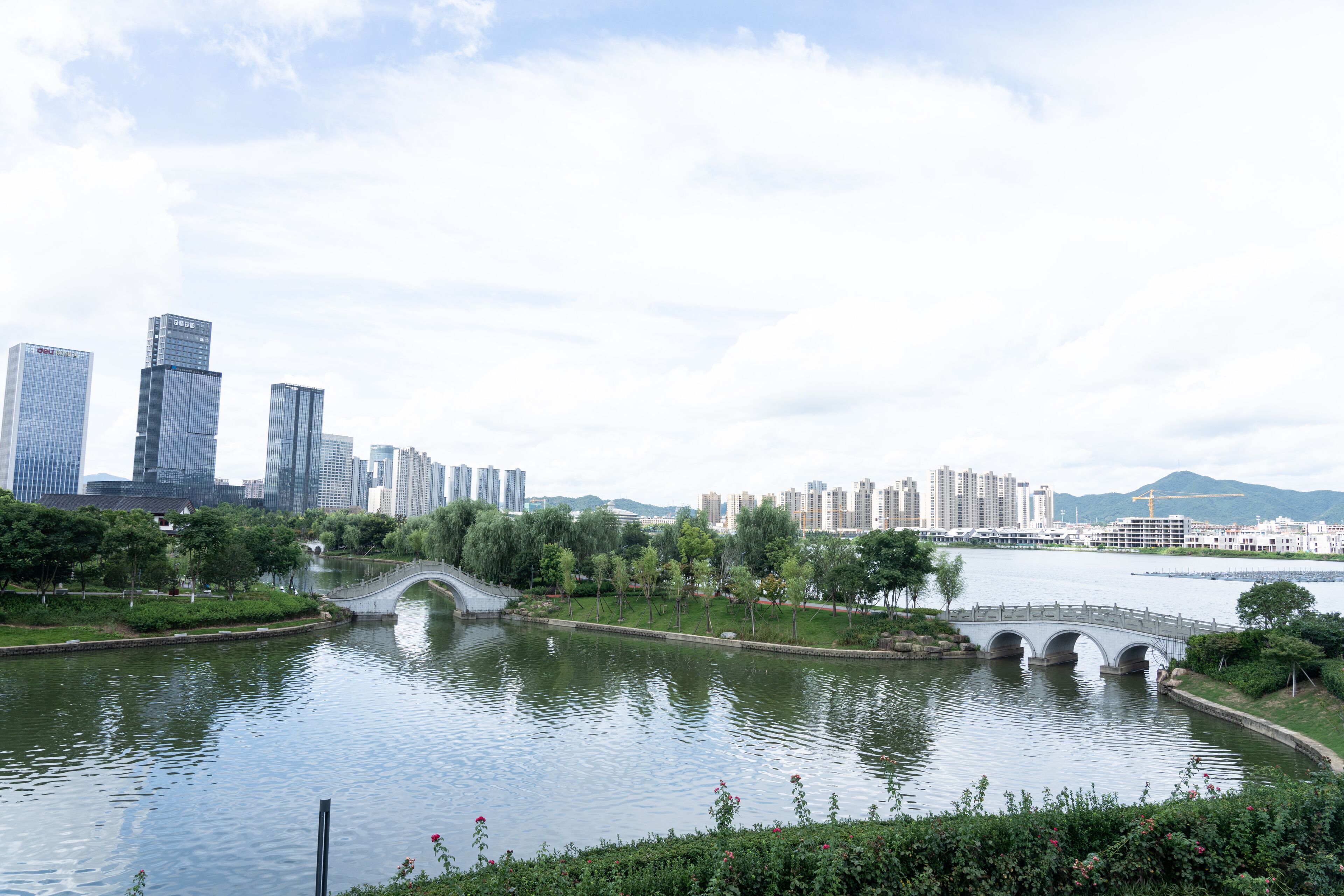 A river with a bridge, surrounded by greenery and buildings in the background.