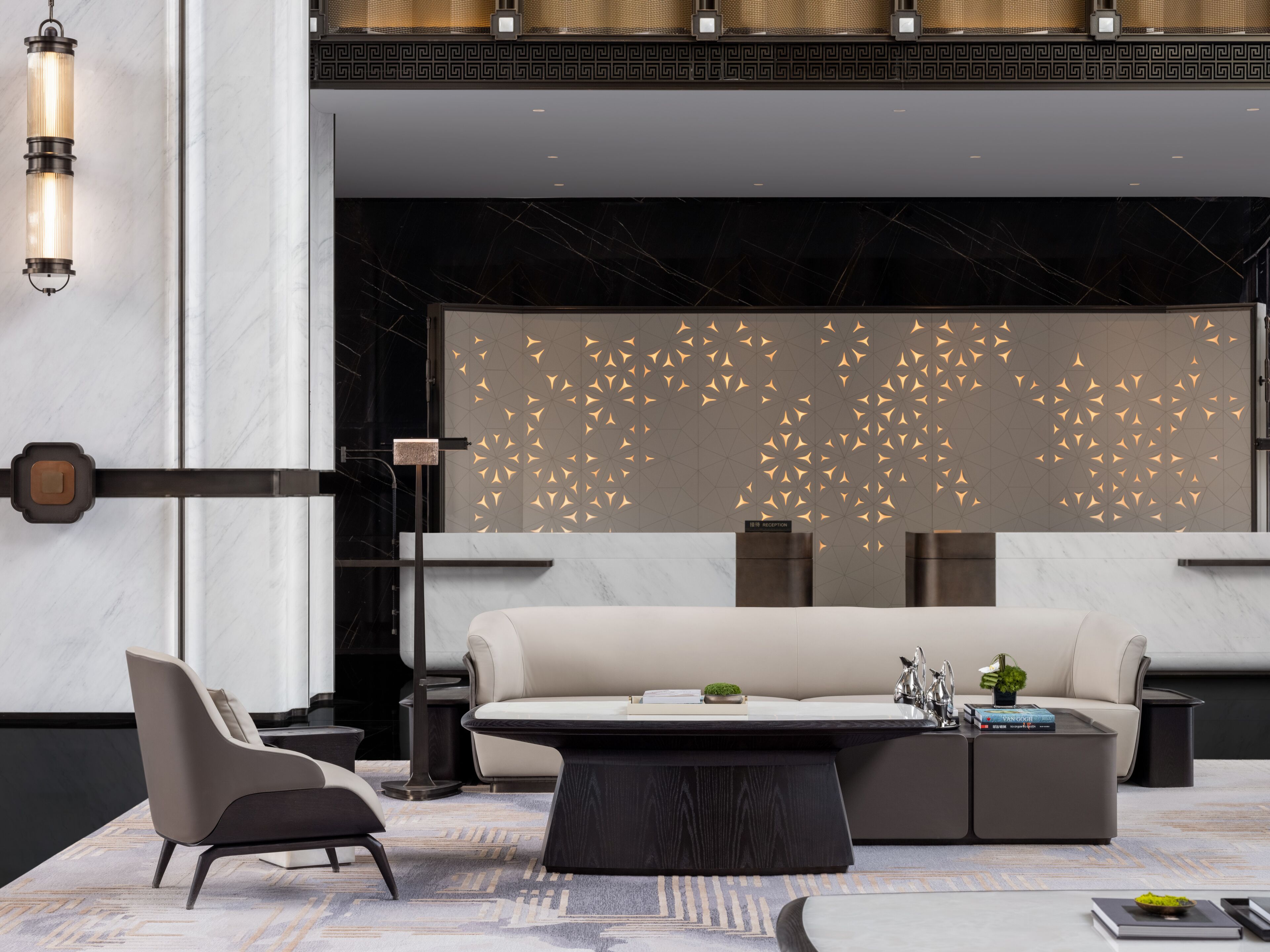 A modern living room with a sofa, coffee table, and chairs, featuring a geometric wall design and a marble floor.