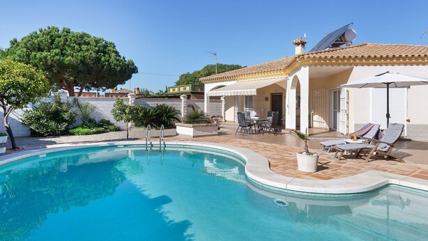 A swimming pool with a curved edge, surrounded by a patio area with lounge chairs and a table.