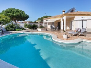 Una piscina con borde curvo, rodeada por un patio con sillones de descanso y una mesa.