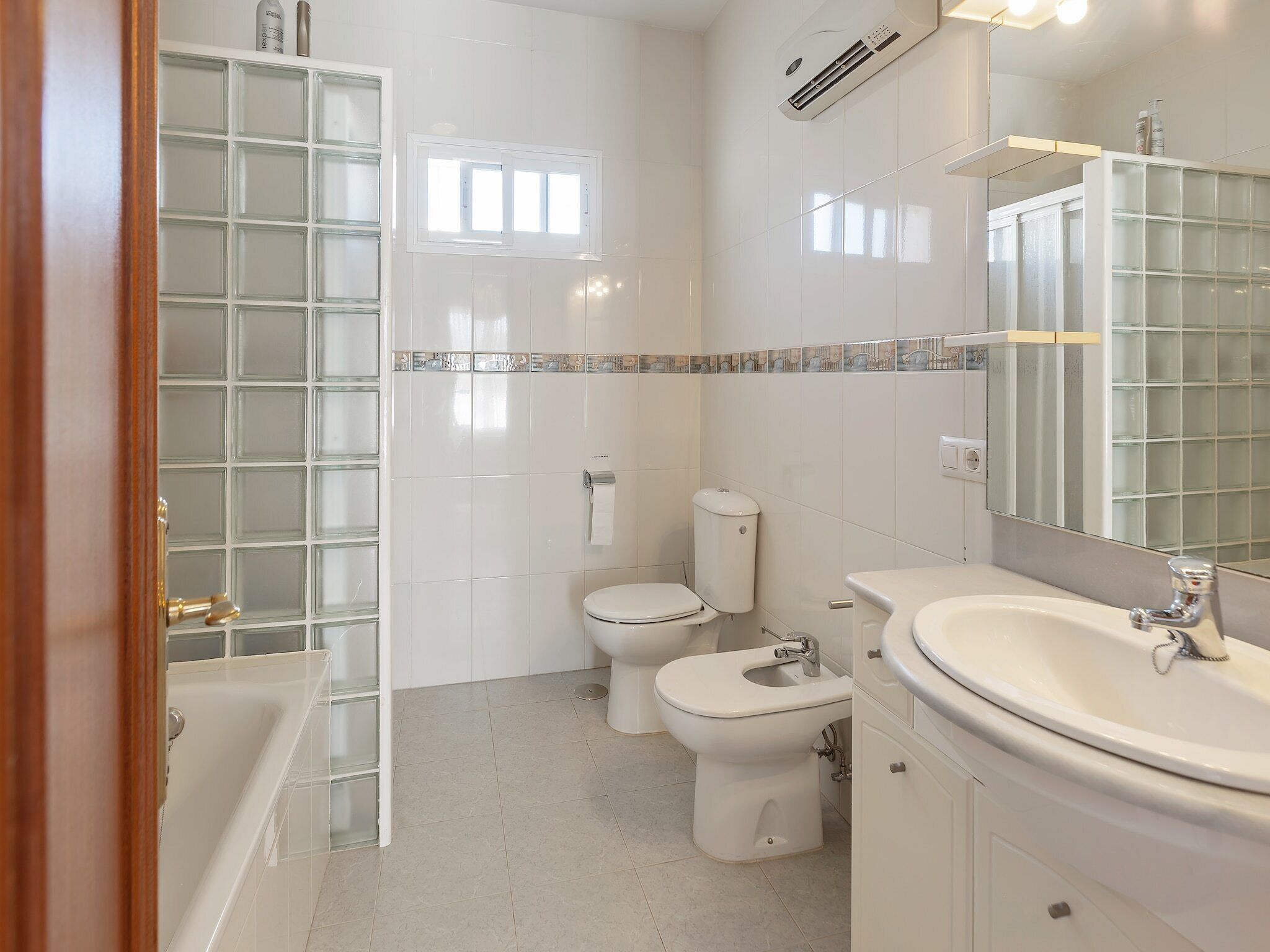 Un bany modern amb un plat de dutxa de vidre, un vàter i un lavabo amb un mirall a la part superior.