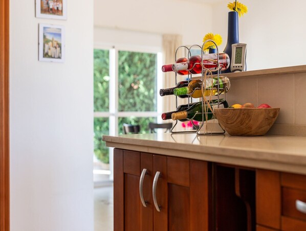 Una encimera de cocina con una botellera que contiene varias botellas, un termómetro y un cuenco de fruta.