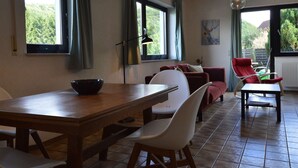 A dining area with a wooden table, white chairs, and a bowl on the table. There is a red sofa and a red chair in the background. - Modern Holiday Home in Eifel with Sauna (Stadtkyll)