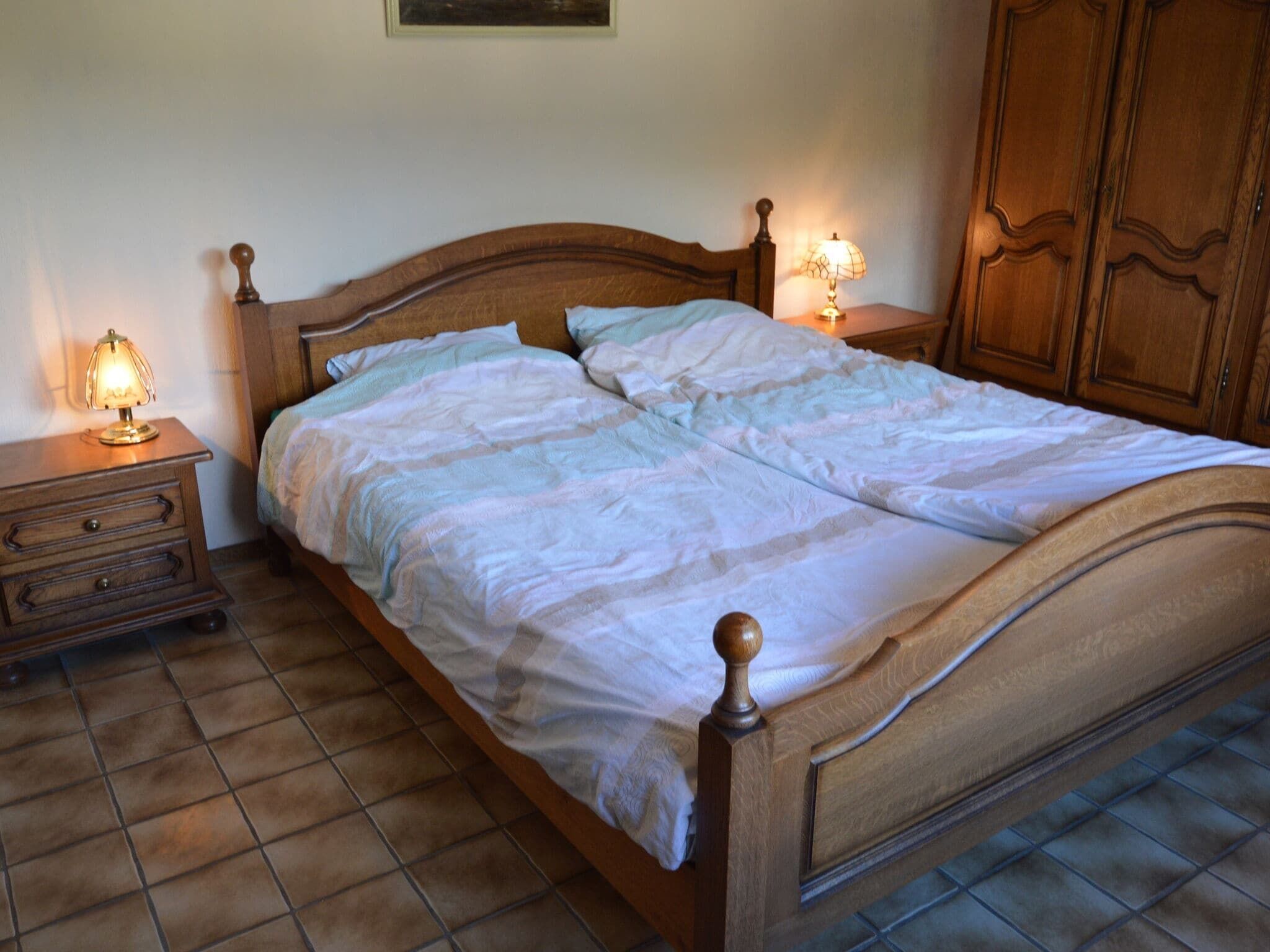 A wooden bed with a headboard, two bedside tables with lamps, and a wardrobe.