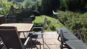 A patio with a table and chairs, a grill, and a hammock. - Modern Holiday Home in Eifel with Sauna (Stadtkyll)