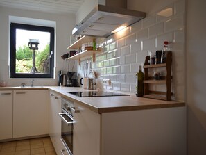 Una cucina moderna con mobili bianchi, forno integrato, macchina da caffè e una finestra che offre vista sul verde.