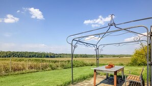A patio with a table and chairs, a metal pergola, and a view of a green field and trees. - Belvilla by OYO Lenze (Staffoli)