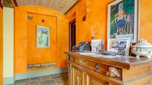 A room with orange walls, a wooden cabinet with carvings, a framed picture, and a vase with flowers. - Belvilla by OYO Lenze (Staffoli)