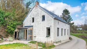 Une maison en pierre blanche avec une véranda en verre, une clôture en bois et une allée pavée.