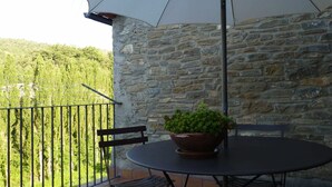 A balcony with a stone wall, a table with a potted plant, a chair, and an umbrella. - Belvilla by OYO Casa Vella (Castigaleu)