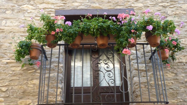 A stone building with a balcony featuring wrought iron railings and terracotta flower pots with pink and purple flowers. - Belvilla by OYO Casa Vella (Castigaleu)