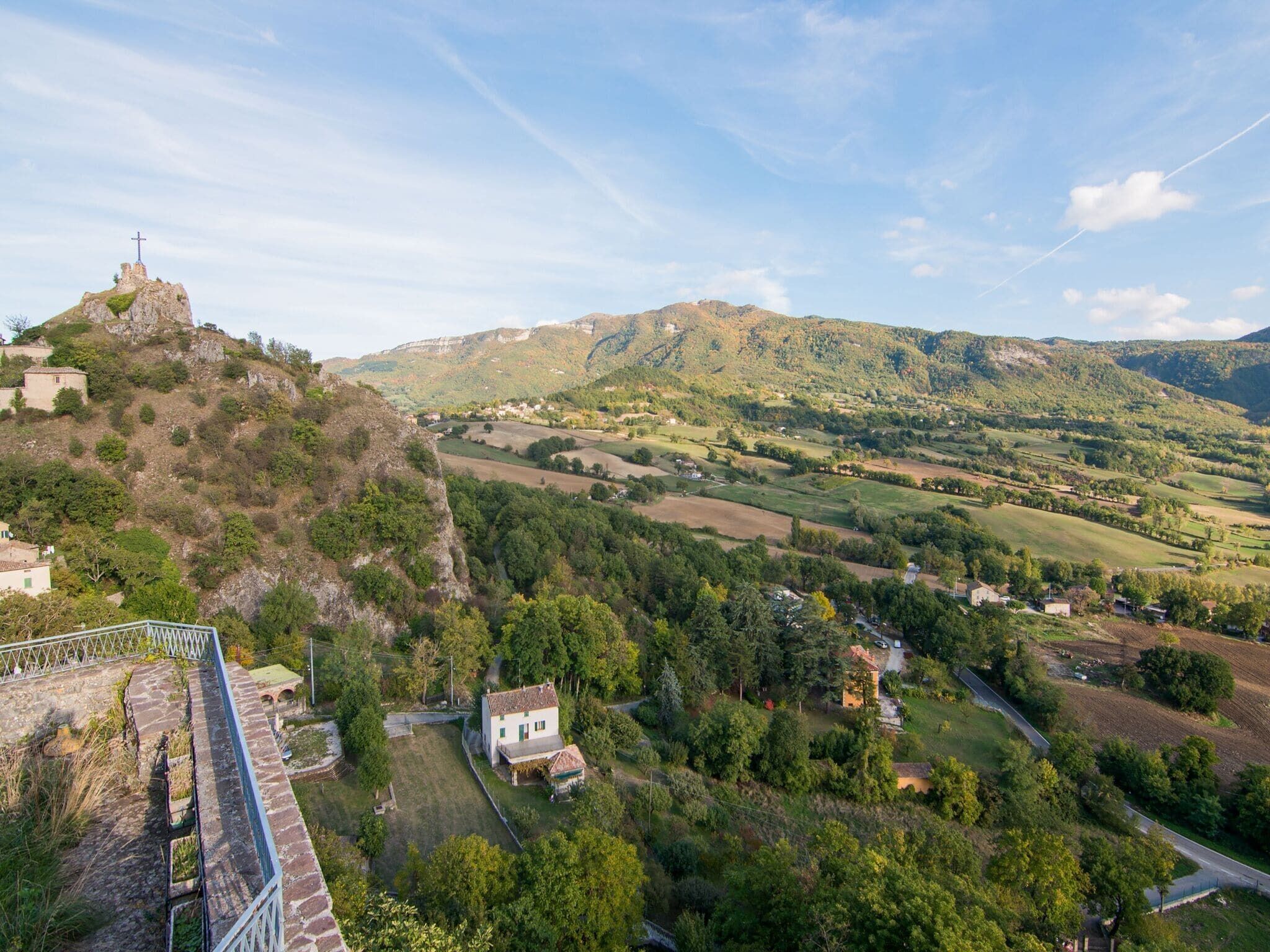 Un paysage rural caractérisé par une colline imposante surmontée d’une croix, un pont de pierre et des maisons dispersées.