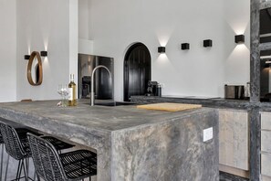 Une cuisine moderne dotée d’un grand îlot central, de tabourets de bar, d’une bouteille de vin et d’une machine à café.