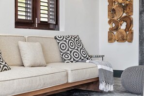 A sofa with patterned cushions, a small side table, and a wall-mounted wooden art piece. - Costa de la Luz with pool on Laguna Marina (Kralendijk)
