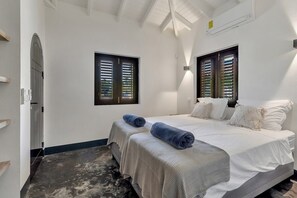 Une chambre avec deux lits, une grande fenêtre et un ventilateur de plafond.