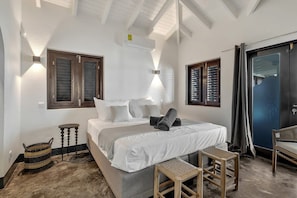 Ein Schlafzimmer mit Bett, Nachttischen, einer Bank, einer Tür und einem Fenster mit Fensterläden.