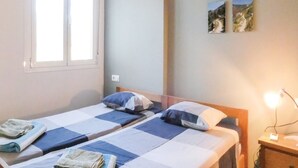 Une chambre avec deux lits, une fenêtre et une table de chevet avec une lampe.