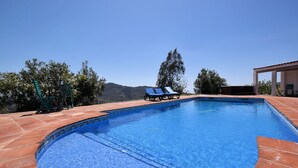 Une piscine dont le bord est revêtu de carreaux, entourée d’une terrasse aménagée avec des chaises et une pergola.