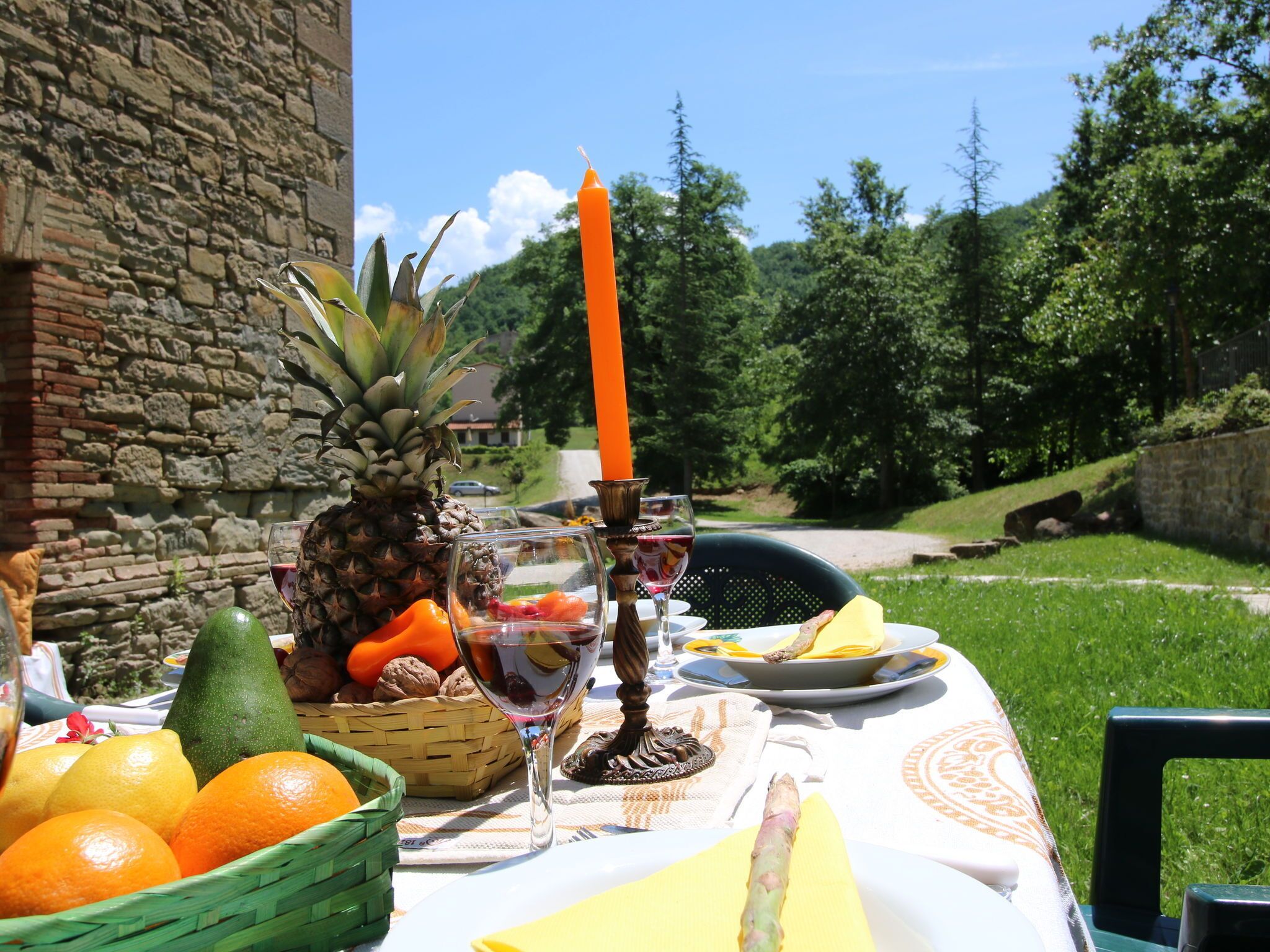 A table set outdoors with fruits, wine glasses, and a candle.