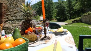 Una mesa al aire libre con frutas, copas de vino y una vela.