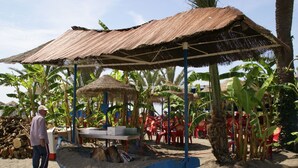 A beachside restaurant with a thatched roof and outdoor seating.