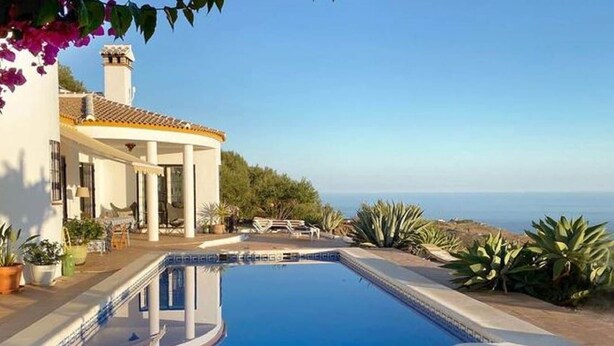 A swimming pool with a curved edge, a patio area with outdoor furniture, and a view of the ocean.