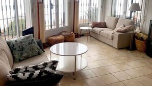 A spacious living room with a sofa, a round table, and a large window with blinds.