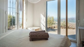 A bedroom with a large bed, a small table, and a view of a rocky landscape through large windows.