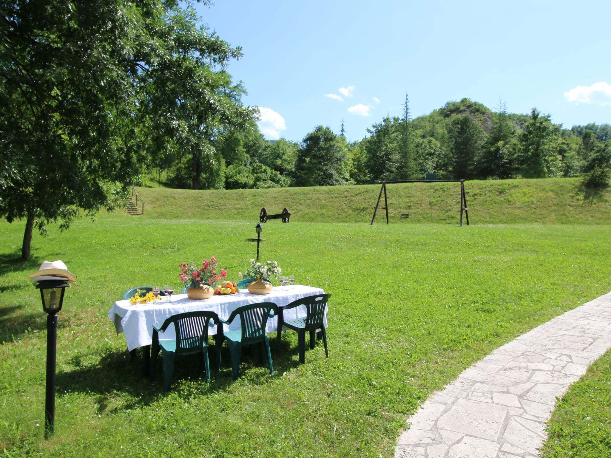 An outdoor dining area with a table set for four, surrounded by chairs, in a grassy field with a stone pathway.