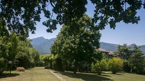 A well-maintained garden with a stone pathway leading to a building with a tiled roof, surrounded by lush trees and a mountain backdrop. - Farmhouse Villa w/ Pool (Cagli)