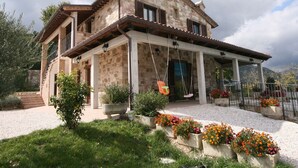 A stone house with a covered porch, outdoor seating, and flower beds. - Farmhouse Villa w/ Pool (Cagli)