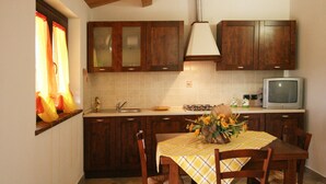 A kitchen with wooden cabinets, a sink, a stove, a television, and a dining table with chairs. - Villa in Cagli with Pool & Scenic Trails (Cagli)