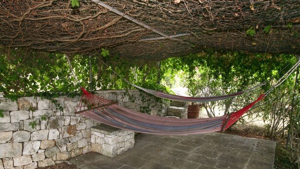 A hammock under a stone wall in a garden setting. - Cottage in Cisternino with Garden & BBQ (Cisternino)