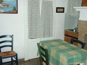 A small kitchen with a table and chairs, a window with floral curtains, and a painting on the wall.