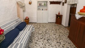 A cozy room with a striped sofa, a small table with a vase, a wooden cabinet, and a tiled floor. - Cottage in Cisternino with Garden & BBQ (Cisternino)