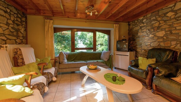 Una habitación acogedora con pared de piedra, techo de madera, un ventanal grande, un sofá, una mesa de comedor y un sillón de cuero.