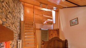 Un dormitorio con cama de madera, pared de piedra, escalera de madera y una ventana pequeña.
