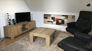 A modern living room with a wooden cabinet, a flat-screen TV, a coffee table, a black leather sofa, and a large abstract painting on the wall.